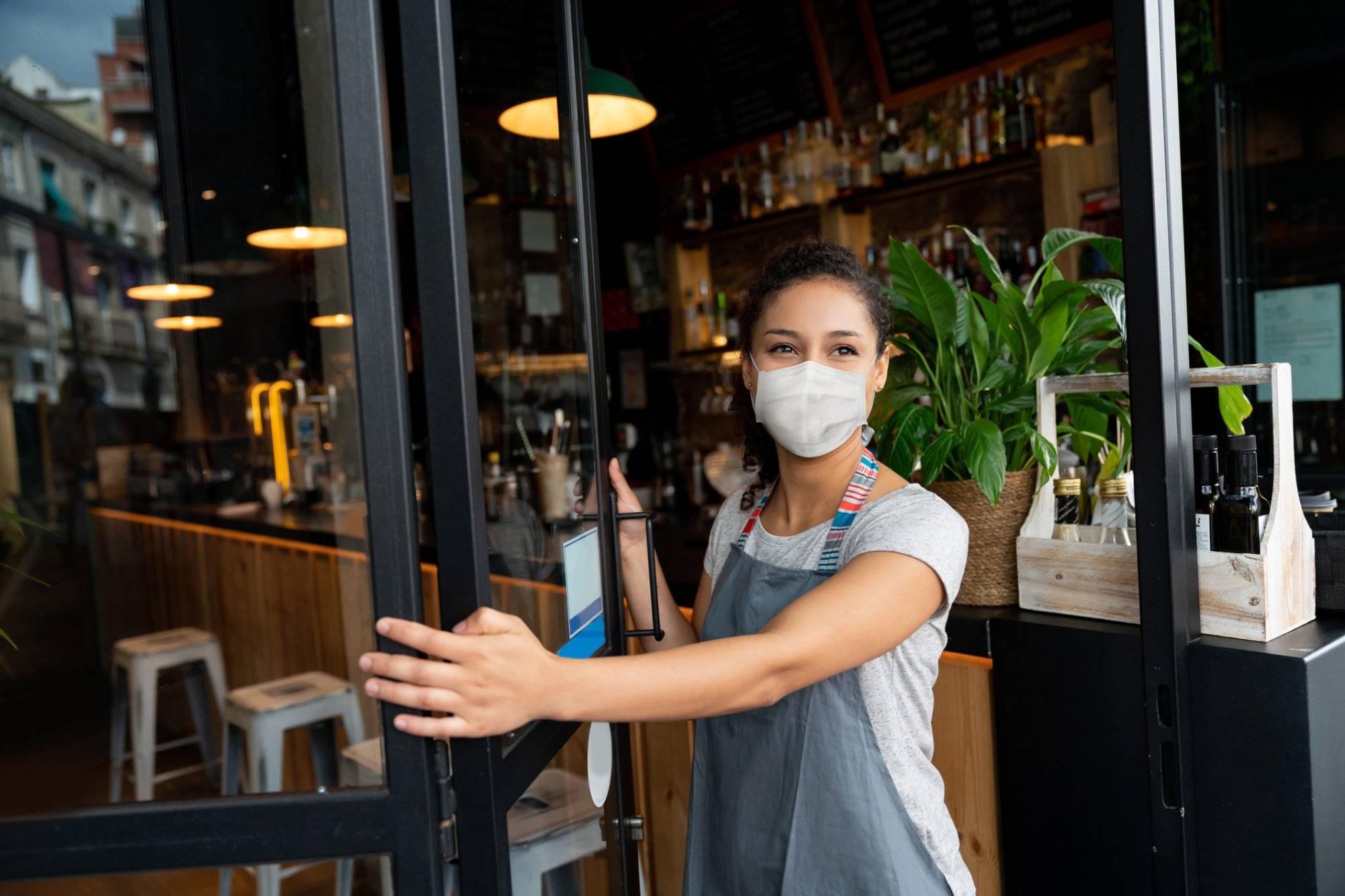 Happy business owner opening the door at a cafe wearing a facemask Happy business owner opening the door at a cafe wearing a facemask