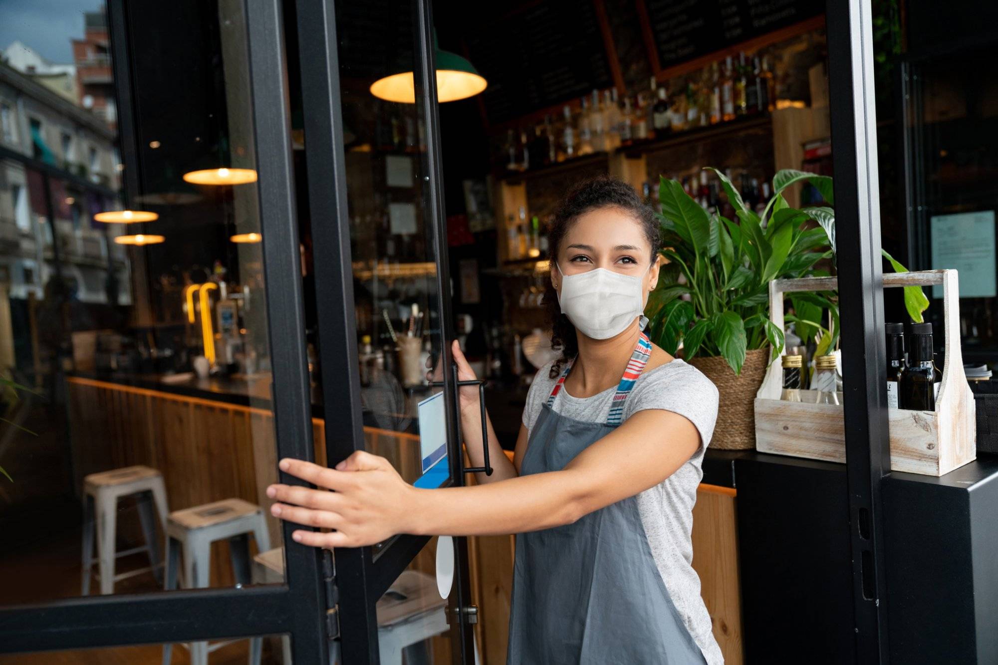 Happy business owner opening the door at a cafe wearing a facemask