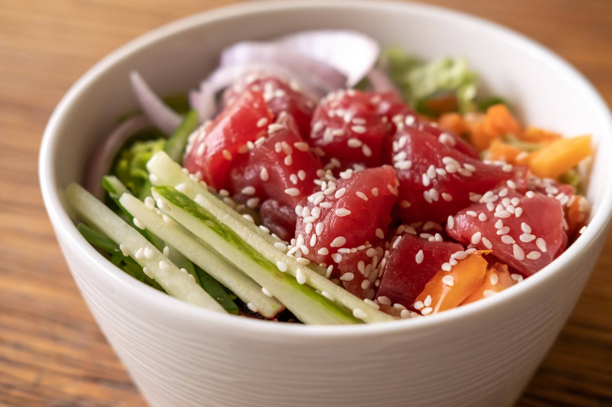 Healthy organic raw tuna poke bowl with cucumber, rice, carrots, onion served in bowl on wooden table. Healthy lifestyle