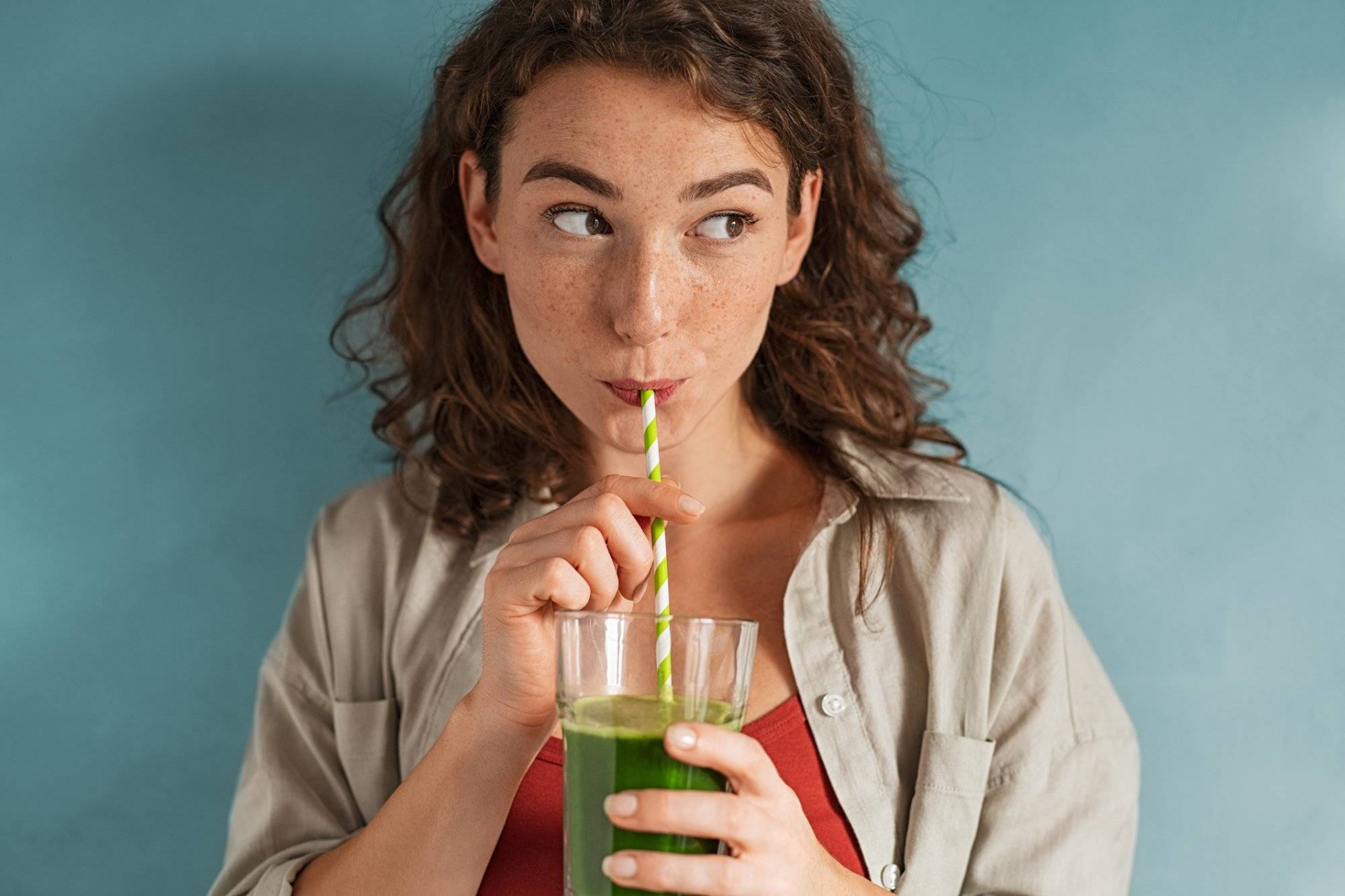 Young woman drinking detox juice with straw on blue wall Young woman drinking detox juice with straw on blue wall
