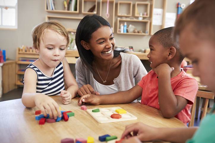 Teacher And Pupils Using Wooden Shapes In Montessori School