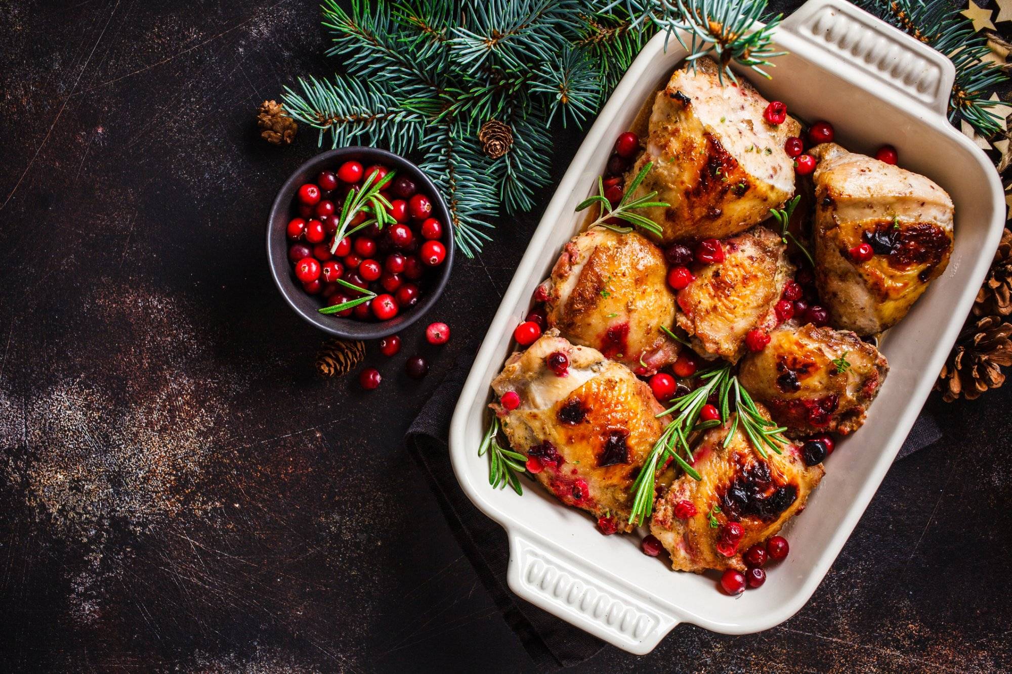 Christmas food. Baked Chicken meat with cranberries and rosemary in the oven dish, dark background, copy space. Christmas food. Chicken meat baked with cranberries and rosemary in the oven dish, top view.