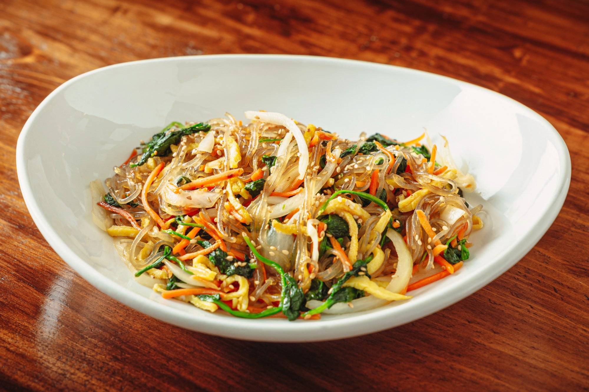 One of Korea's traditional food, Japchae in a white dish. Wood table background.